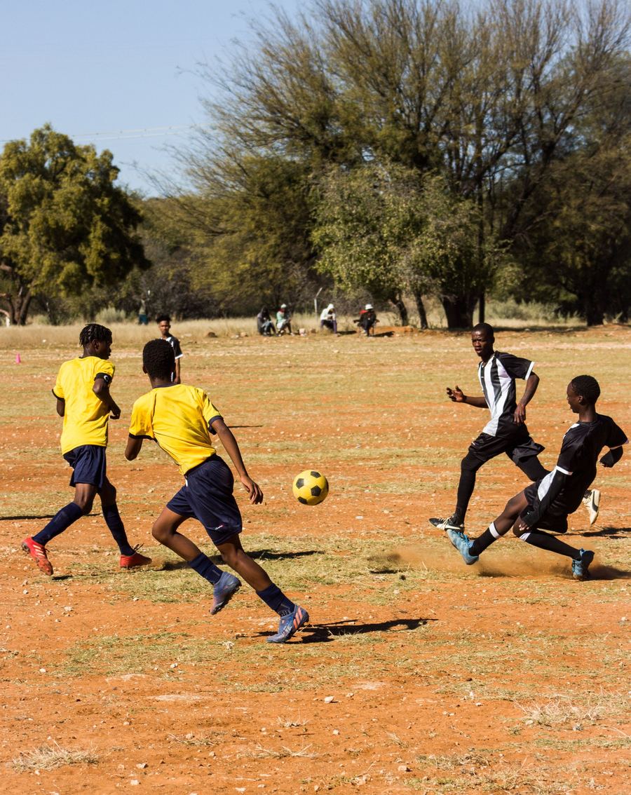 Young players in yellow and black shirts playing football on a dirt pitch