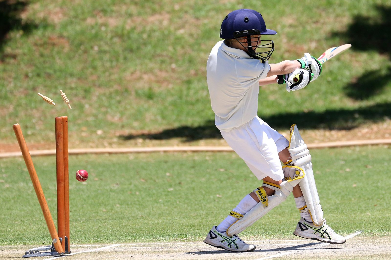 A young batsman playing a shot as the bails fly off the stumps