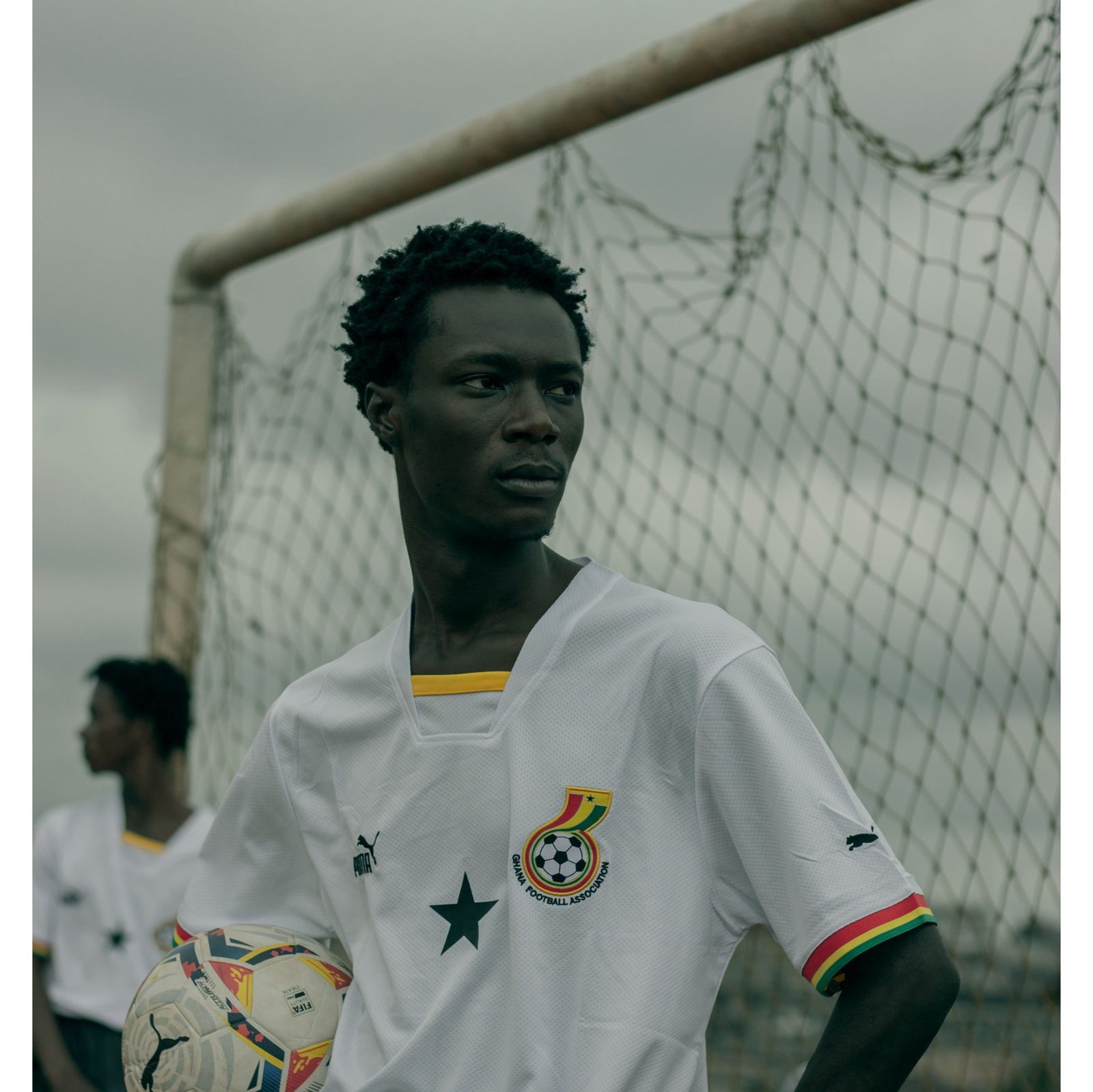 A young footballer in a white Ghana shirt standing by a goal
