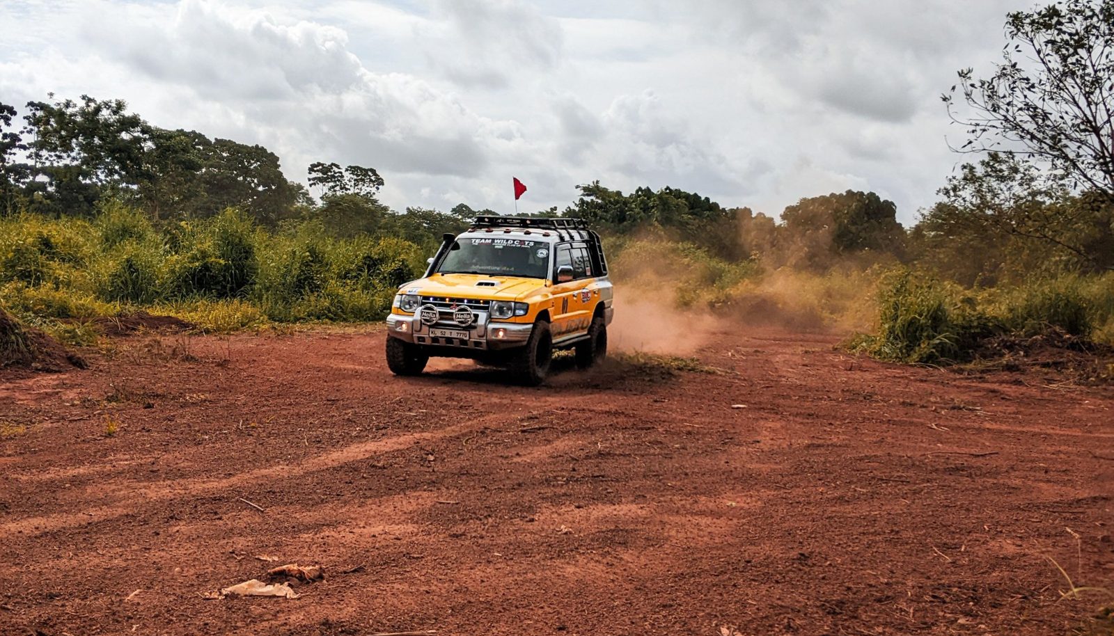 A rally car kicking up dust on a red dirt track