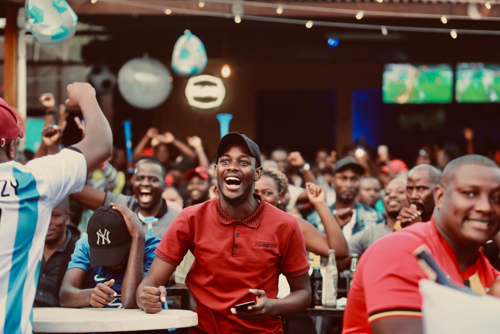 Football fans cheering while watching a match on TV screens